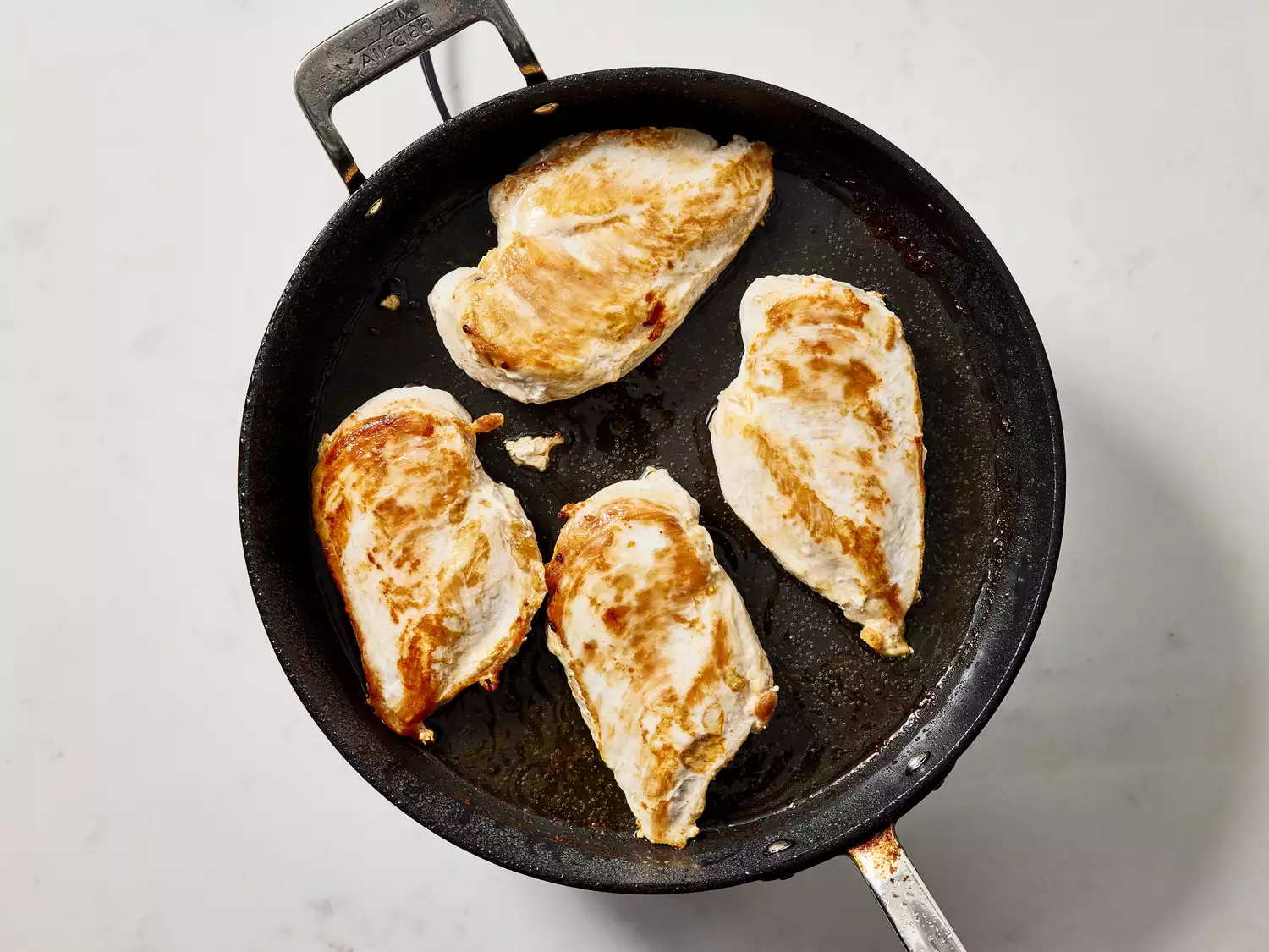 Chicken breasts being seared in a black frying pan.