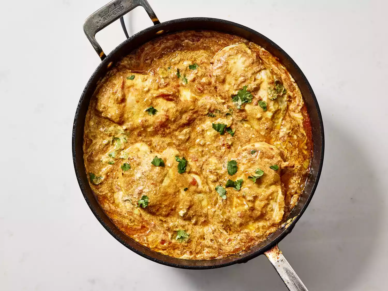 Chicken pieces cooking in a creamy curry sauce.