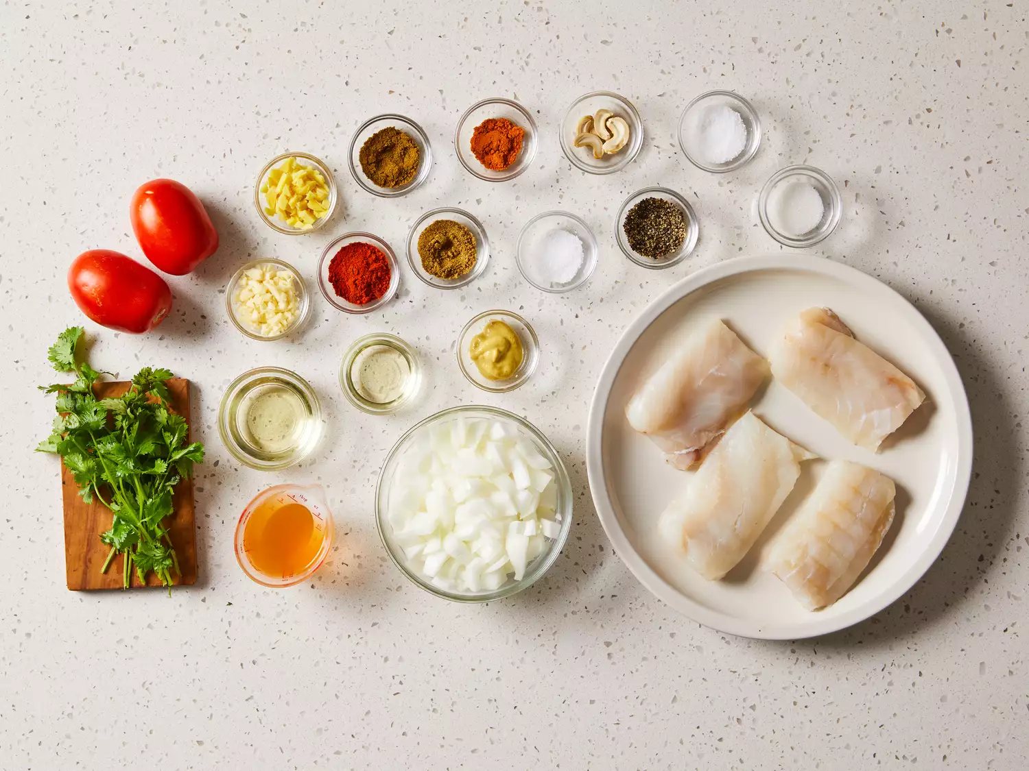 Indian Fish Curry ingredients in glass bowls on a white counter 