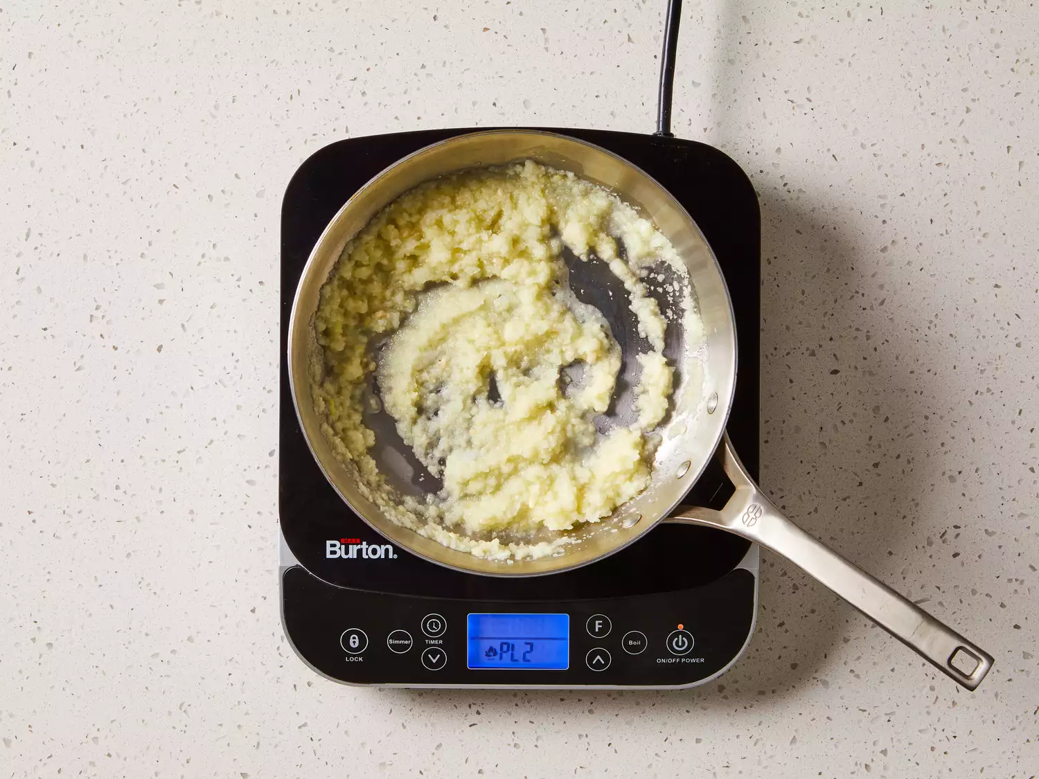 Onion, garlic, ginger, and cashews in a pan on a burner 