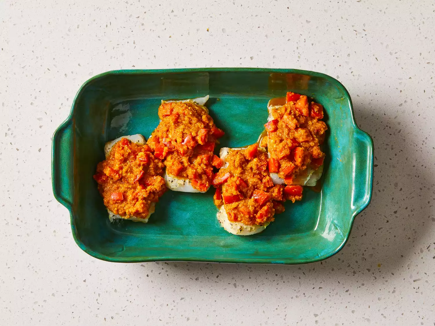 Fish fillets topped with tomato and herb sauce in a green baking dish 