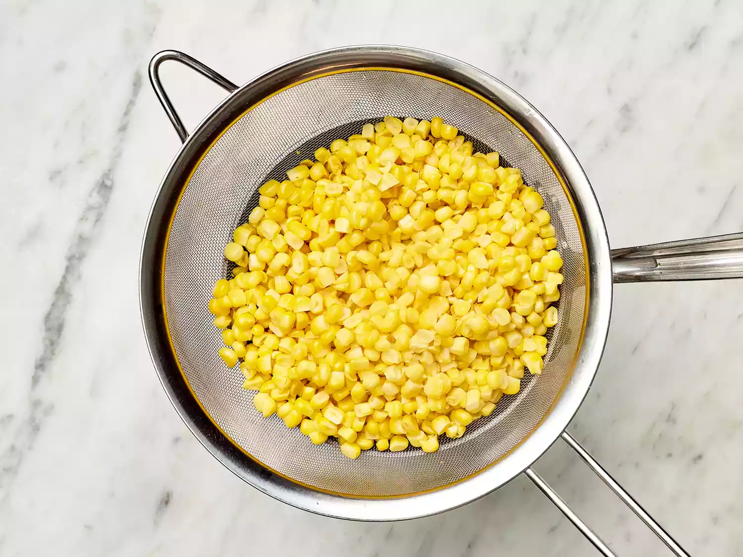 Corn in a colander over a pot 
