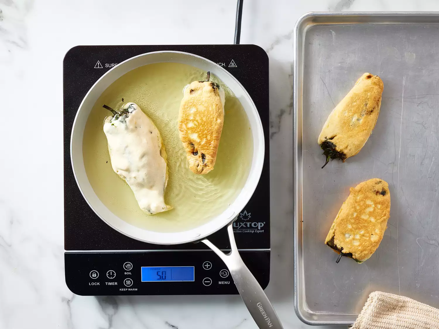 Chiles rellenos being fried in a pan, with some completed ones on a tray