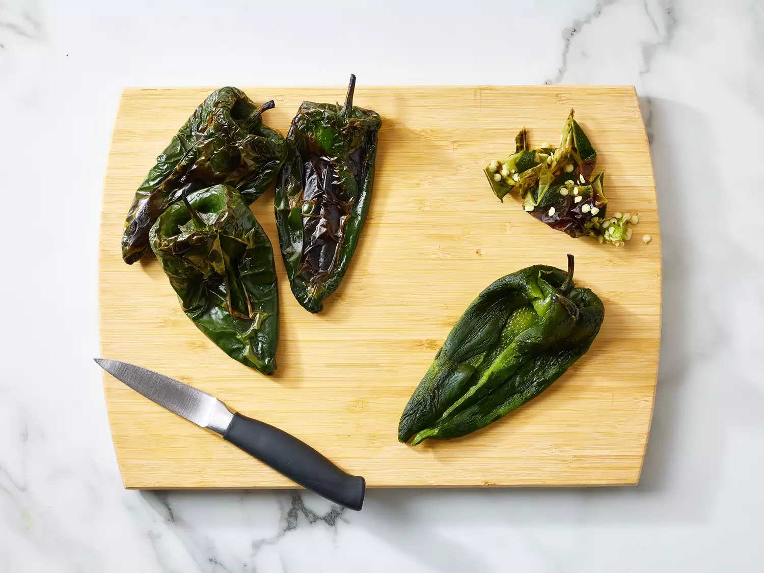 Roasted poblano peppers prepared on a cutting board with a knife nearby