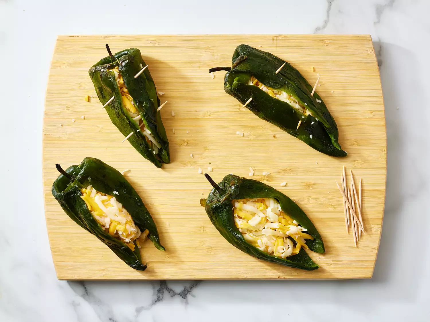 Four poblano peppers stuffed with cheese on a wooden cutting board with toothpicks for securing