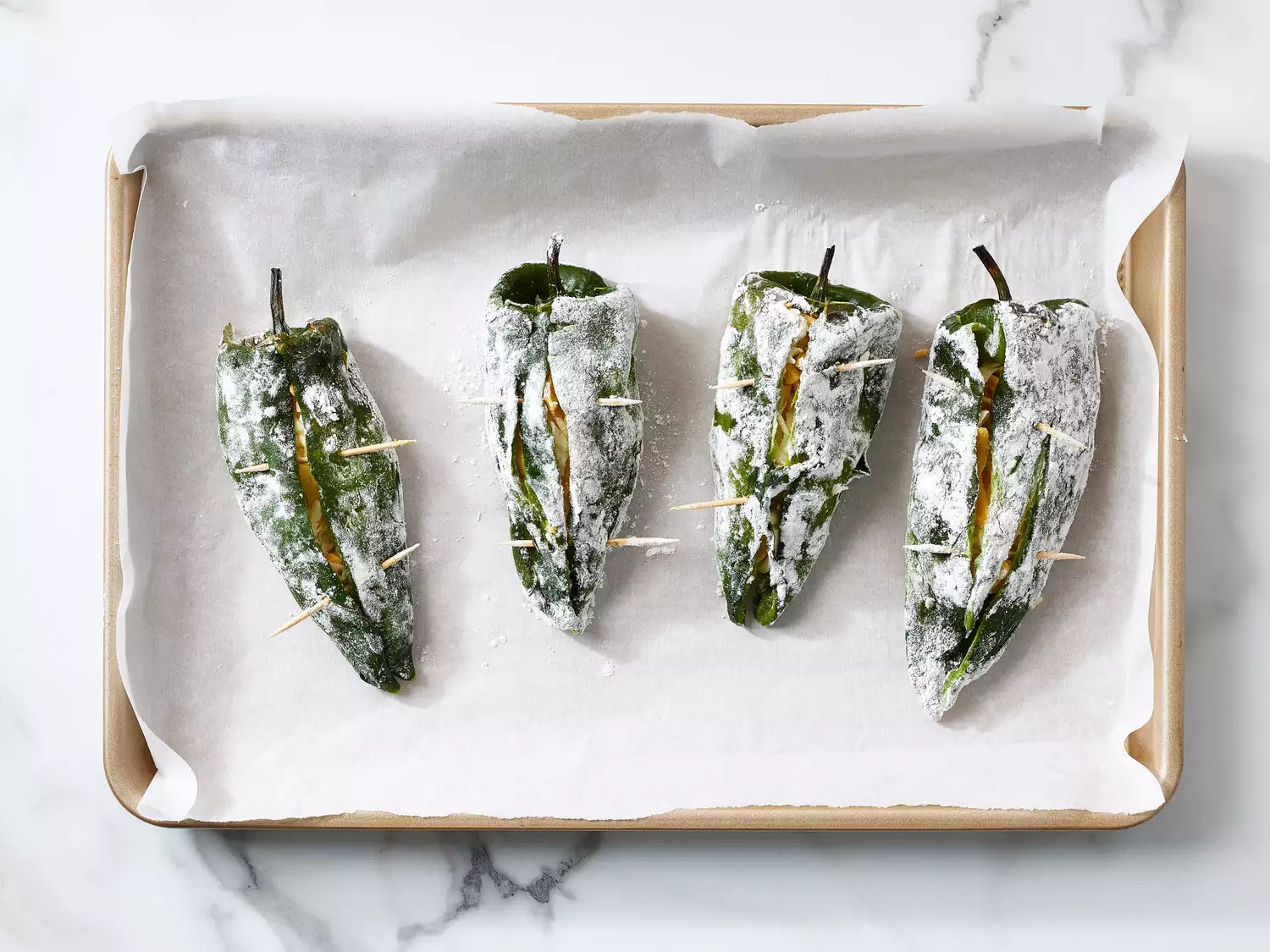 Four stuffed poblano peppers coated with flour on parchment paper lined baking sheet