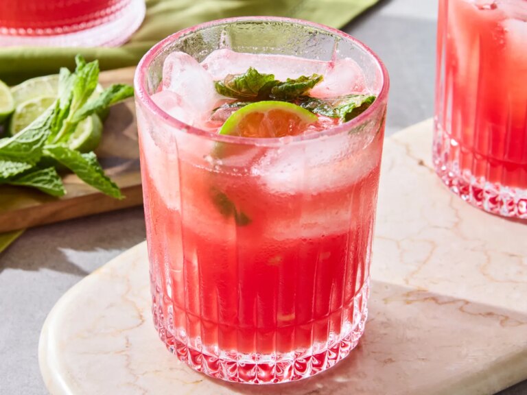 A glass of watermelon agua fresca garnished with mint and lime slice on a marble surface
