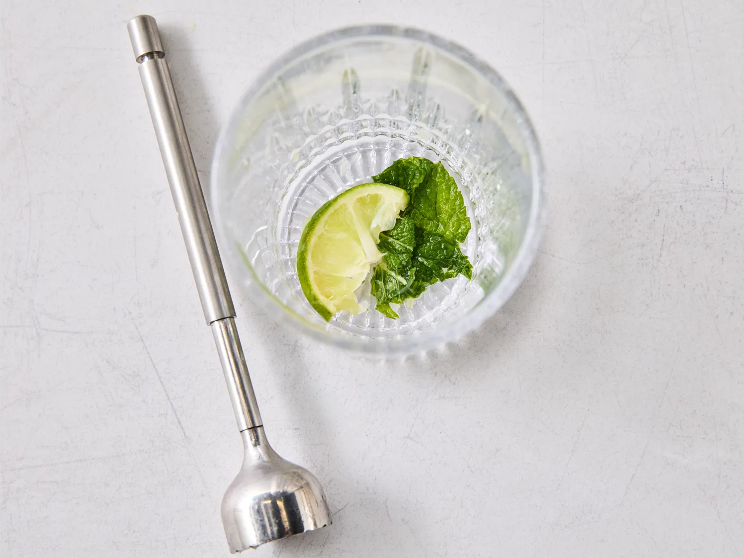 A blending tool next to a glass containing lime and mint leaves