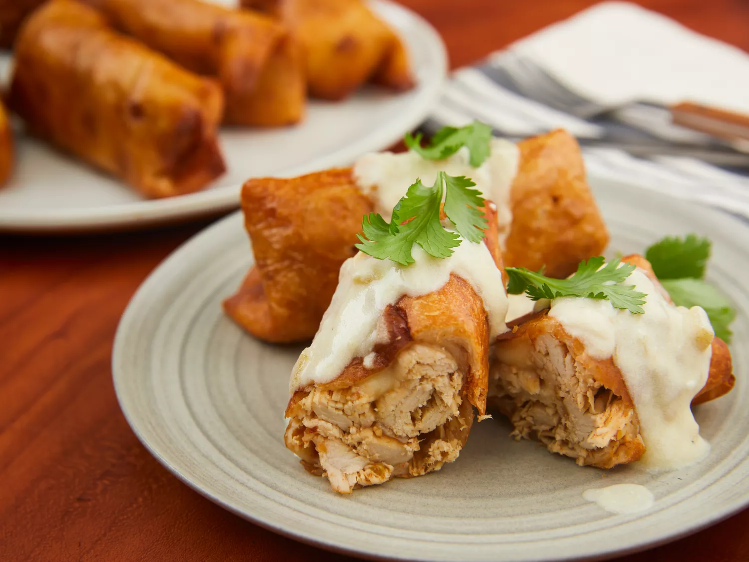 mid angle looking at a plate of chicken chimichangas cut in half and topped with sour cream sauce garnished with fresh herbs 