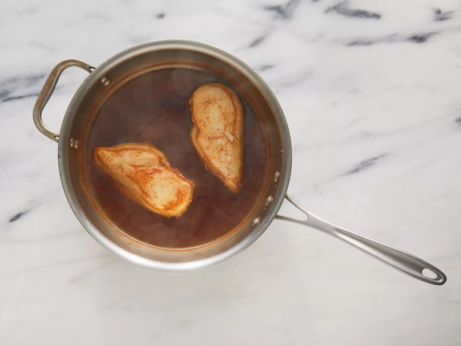 Overhead of chicken cooking in a pot full of water and spices.