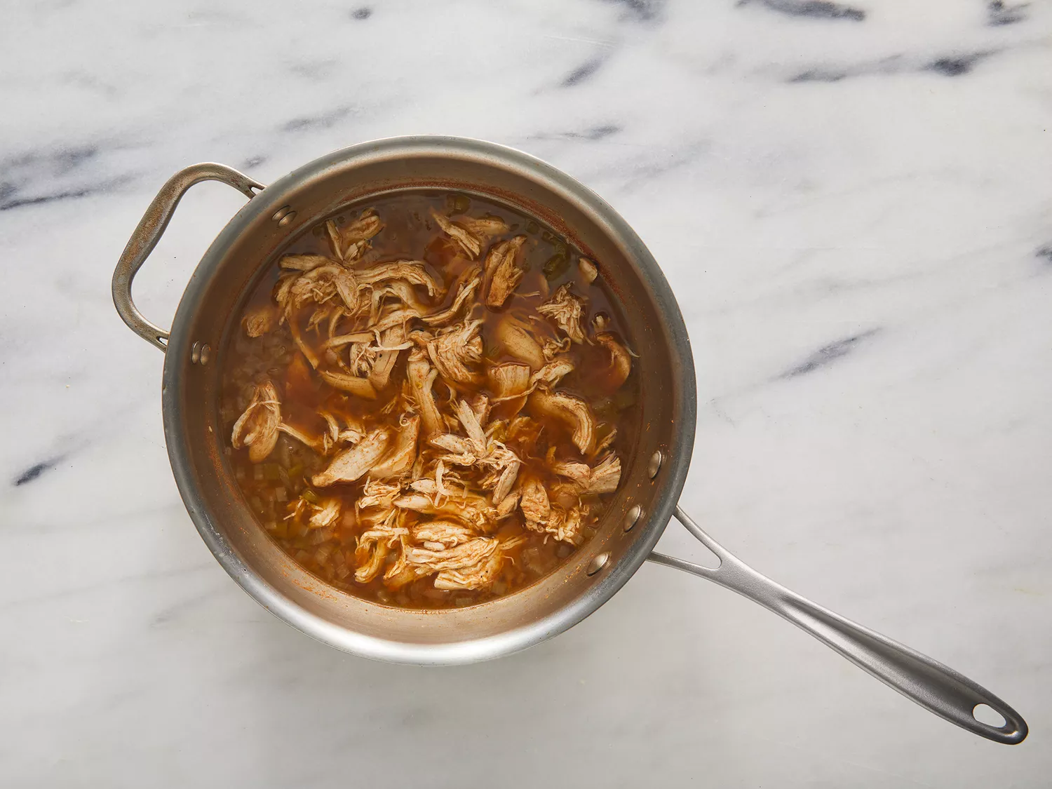 Overhead of shredded chicken mixed in a spices sauce and cooking in a pot. 