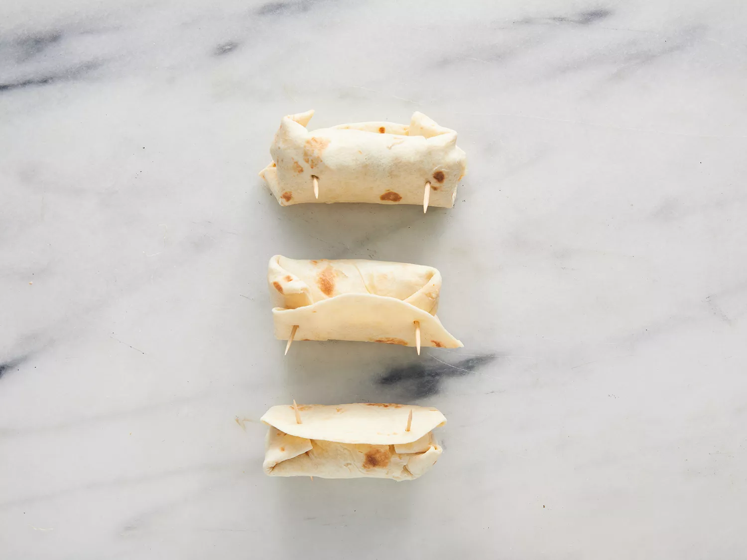 Overhead of three folded chimichangas being help closed by toothpicks. 