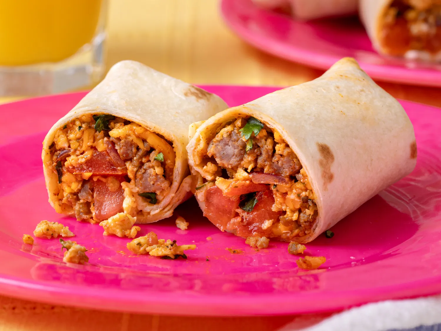 Breakfast burritos cut in half served on a pink plate with visible filling including scrambled eggs sausage and vegetables