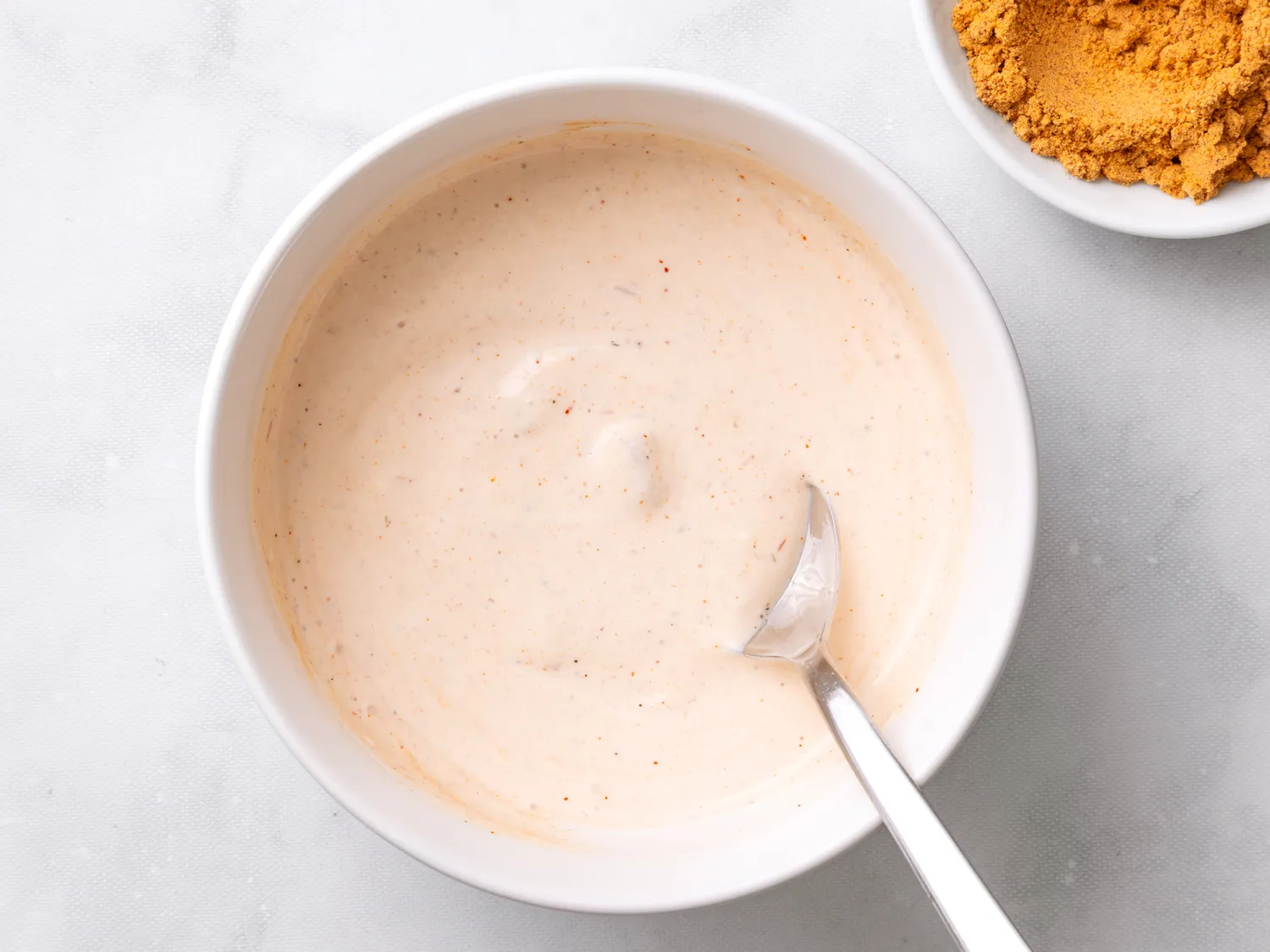 Bowl of ranch-based taco sauce with a spoon beside spices in a smaller bowl