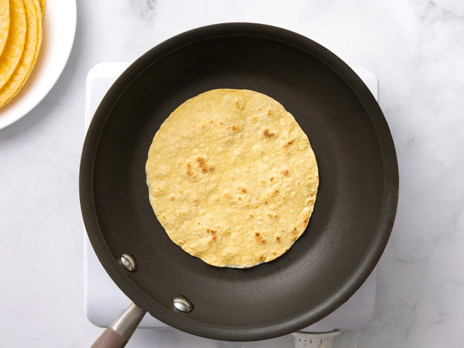 A tortilla being heated in a skillet on a stovetop