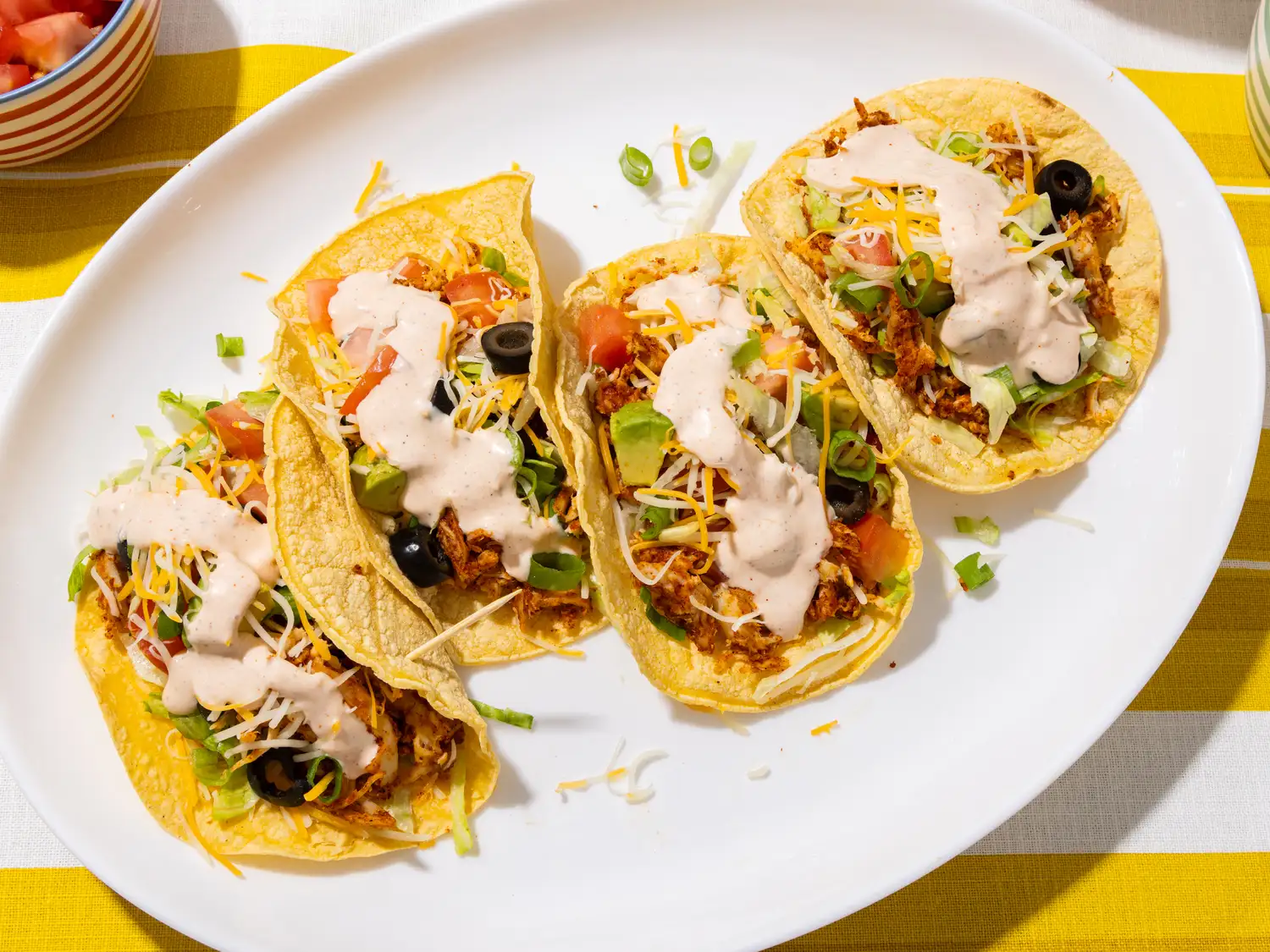Four tacos with shredded chicken, toppings, and creamy sauce on a plate