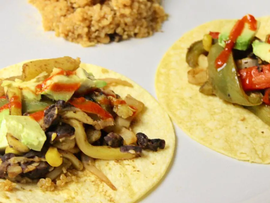Close up view of vegan fajitas with peppers, avocado and red sauce on corn tortillas, served with grains on a white plate