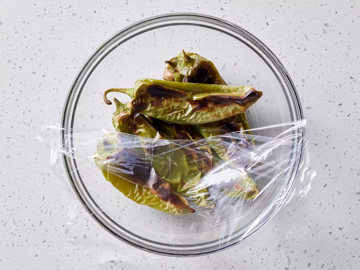 blackened peppers steaming in a bowl as they cool
