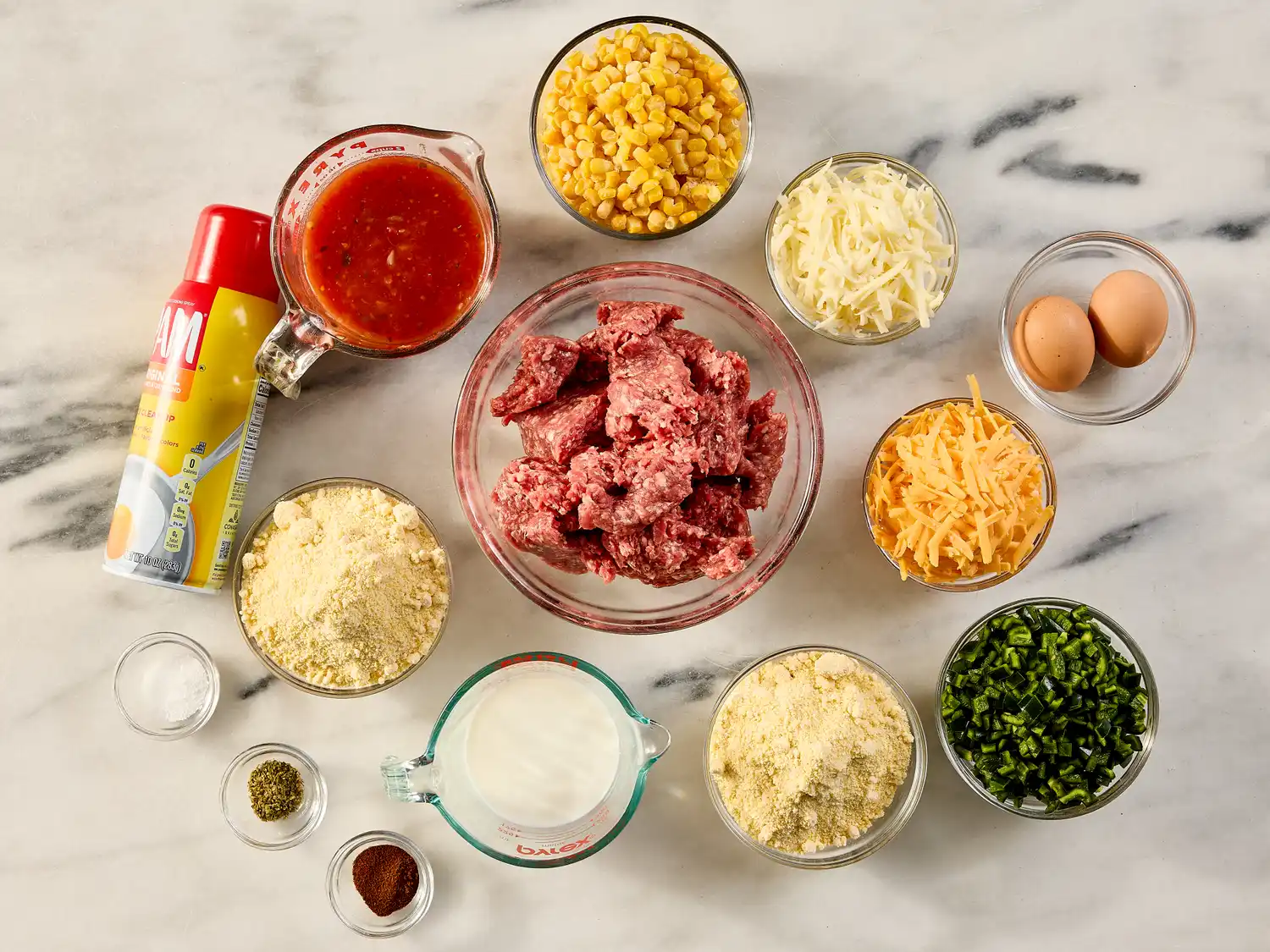 Ingredients for making hot tamale pie laid out on a surface including ground meat cheese corn and various spices