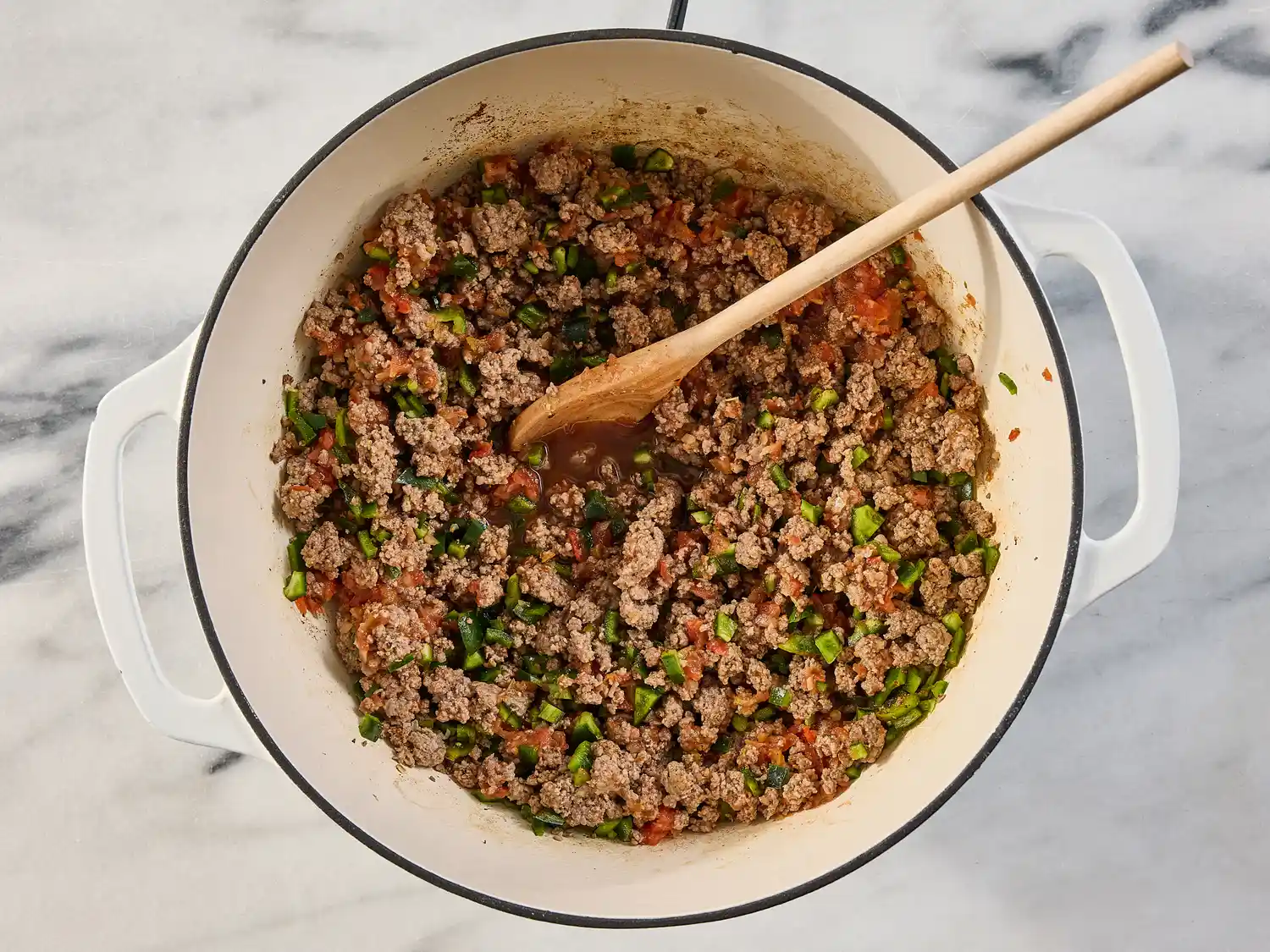 A pot filled with ground meat vegetables and a wooden spoon ingredients for a recipe being prepared