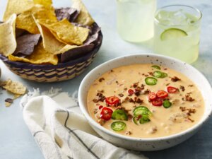 Close up view of chorizo queso dip garnished with peppers in a bowl, served with tortilla chips in a basket