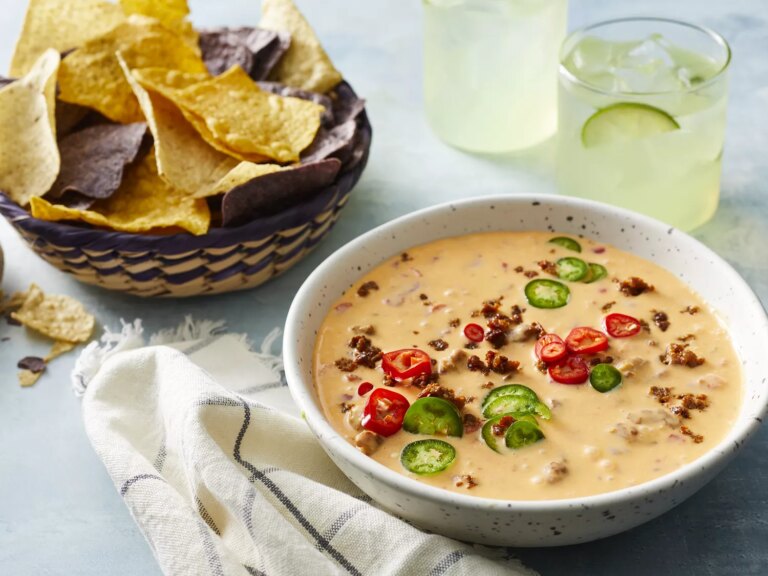 Close up view of chorizo queso dip garnished with peppers in a bowl, served with tortilla chips in a basket