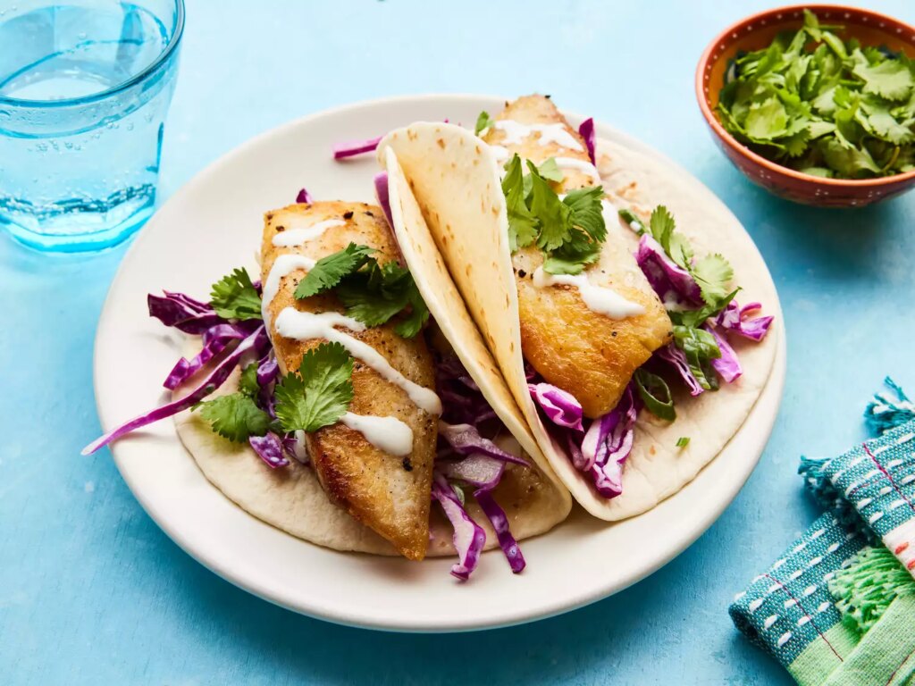 Looking at a plate of two fish tacos, garnished with cilantro