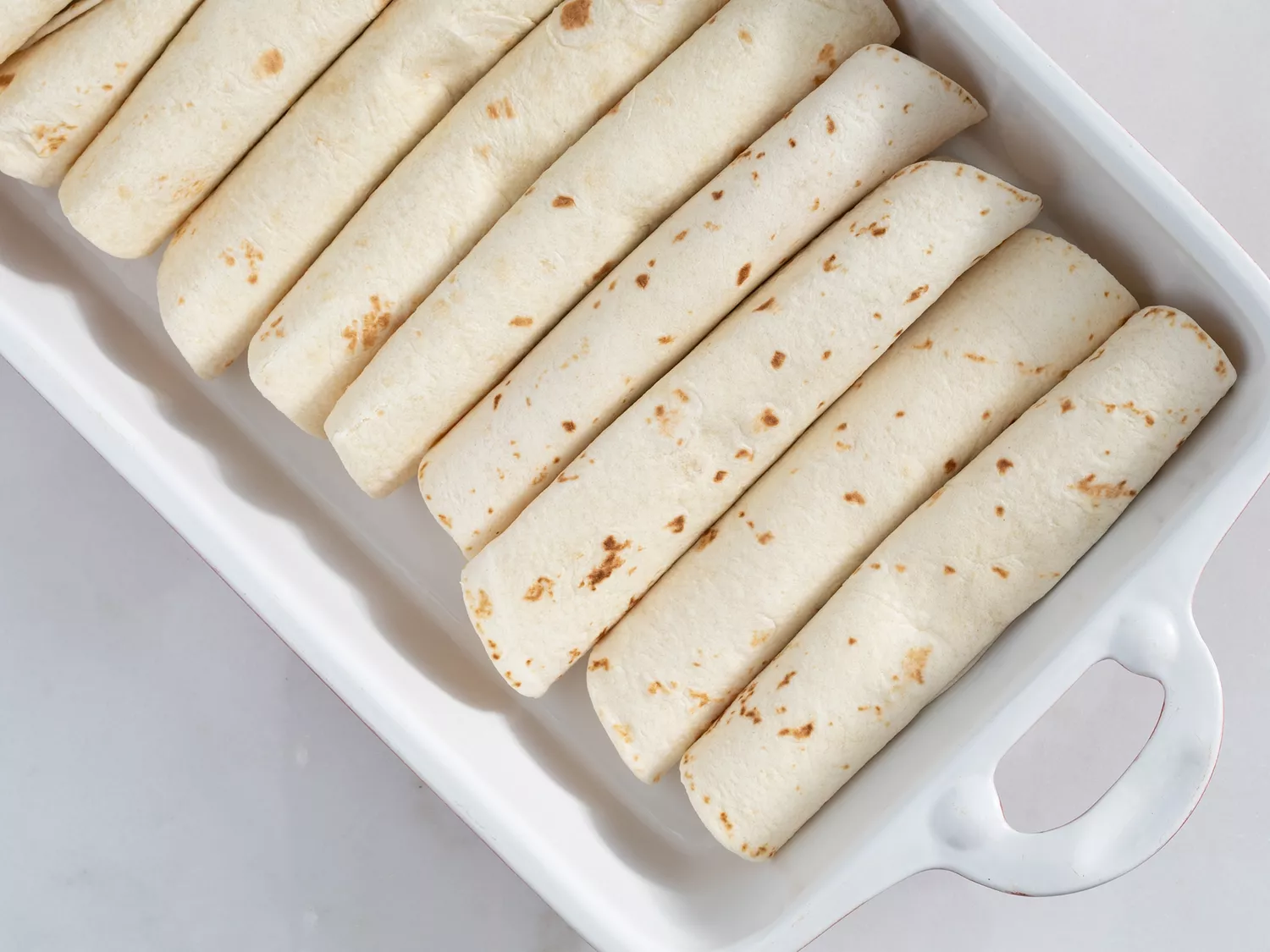 Rolled flour tortillas placed in a baking dish 