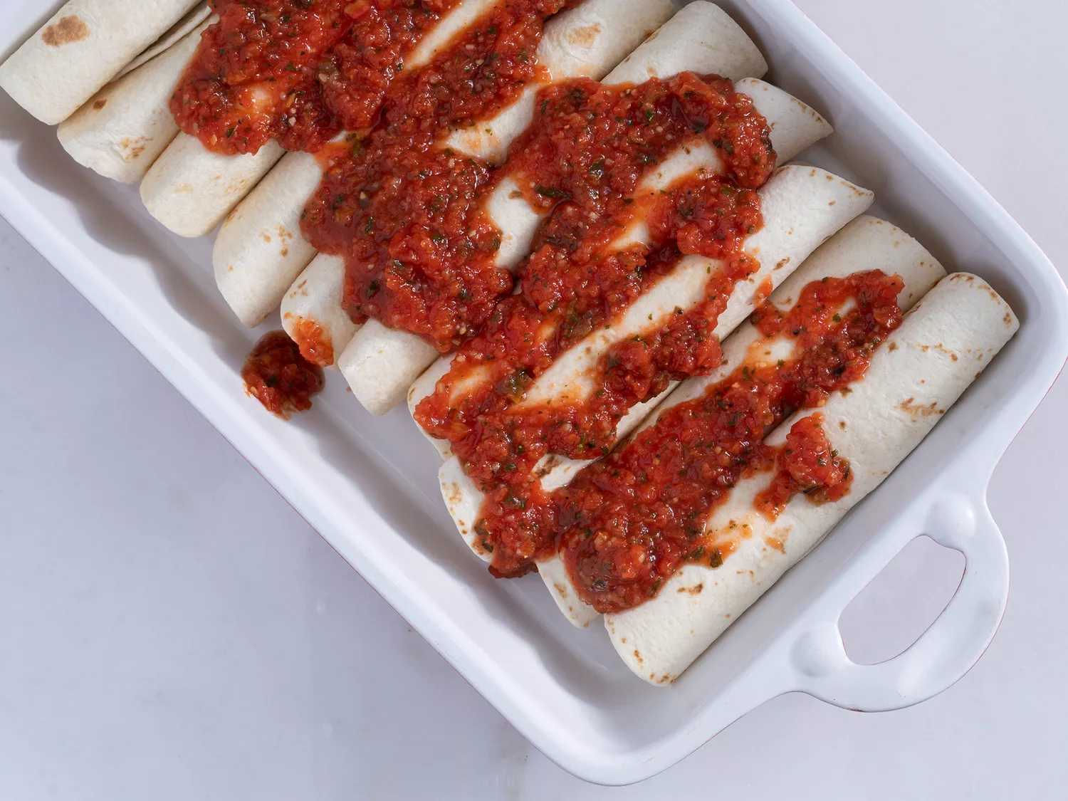 Red salsa spread over the top of rolled flour tortilla enchiladas 