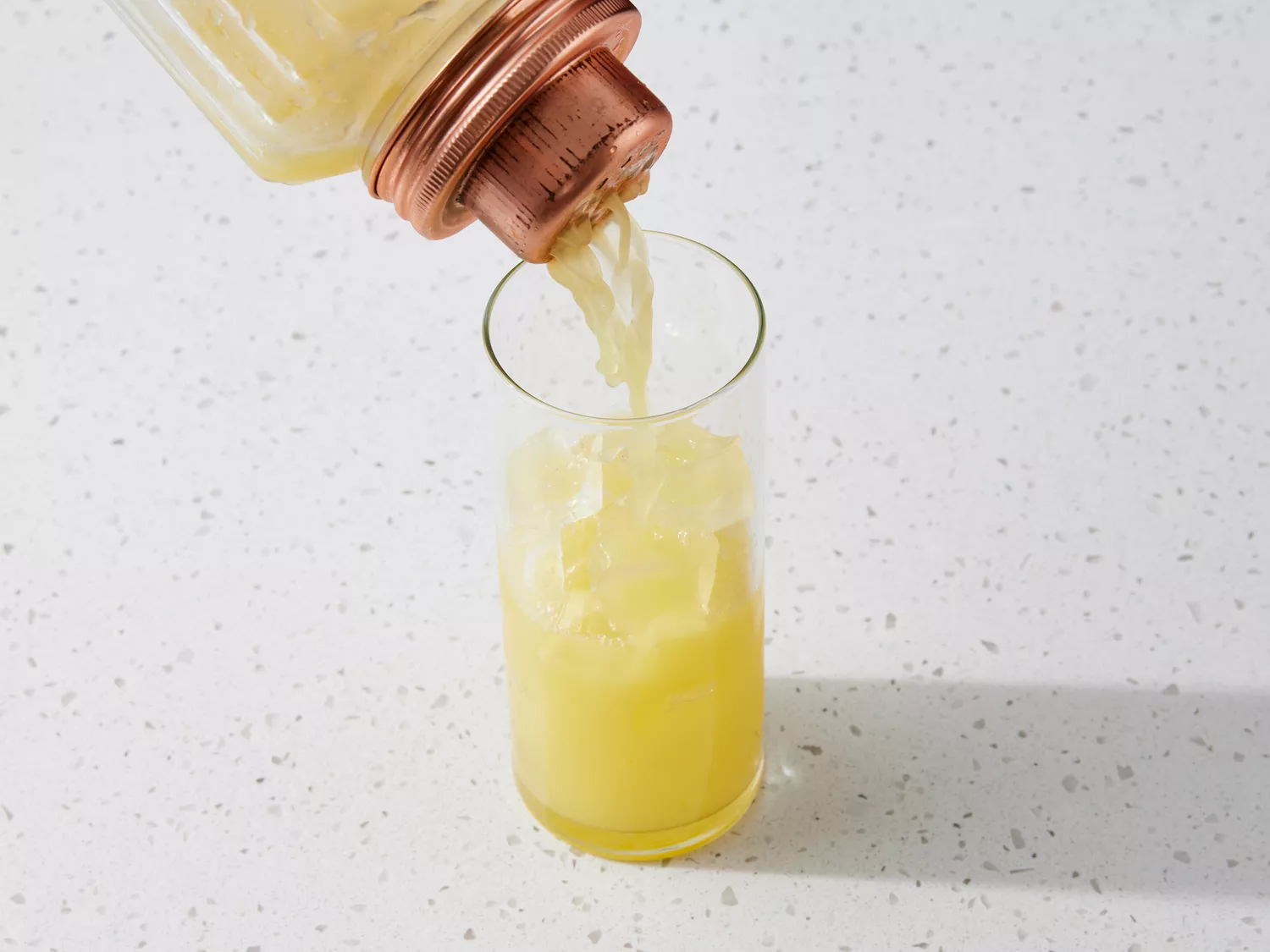 Orange juice and tequila poured from a cocktail shaker into a glass with ice 