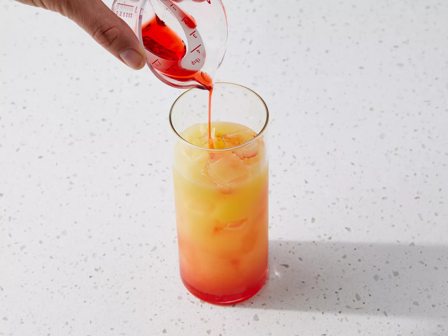 Hand pouring grenadine into a glass with ice, orange juice and tequila