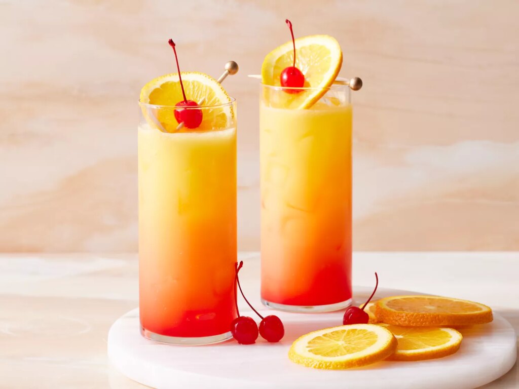 Tequila sunrise cocktails in highball glasses garnished with orange slices and cherries