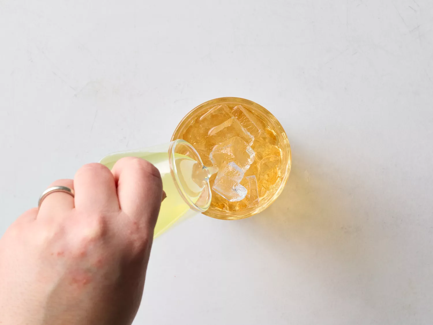 Hand pouring yellow liquid into a glass with orange mixture and ice