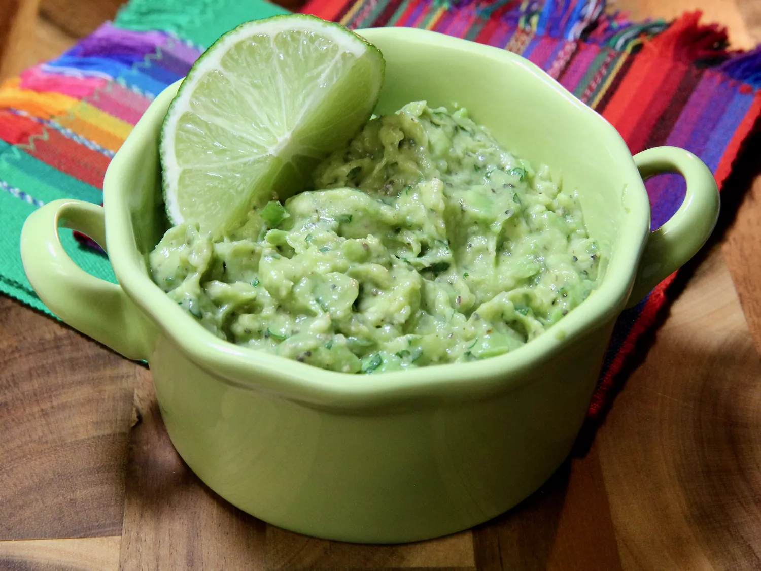 Guacamole in green bowl garnished with lime wedge