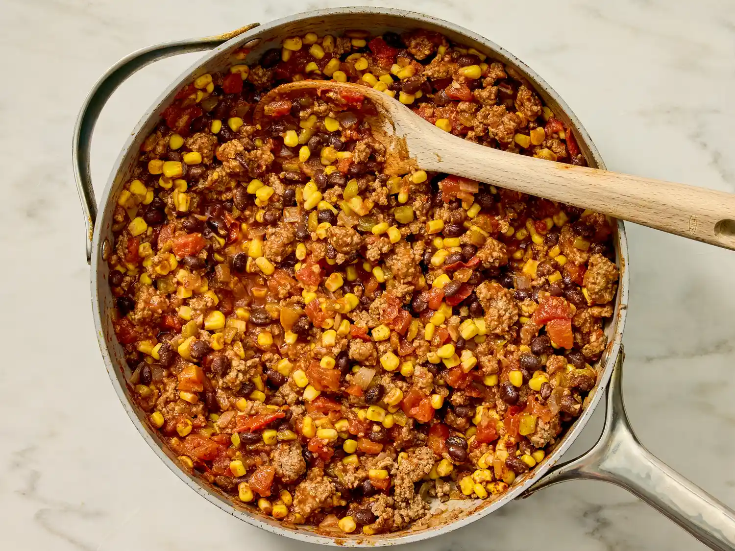 Pan of Mexican quesadilla casserole ingredients being cooked includes corn beans ground meat and tomatoes