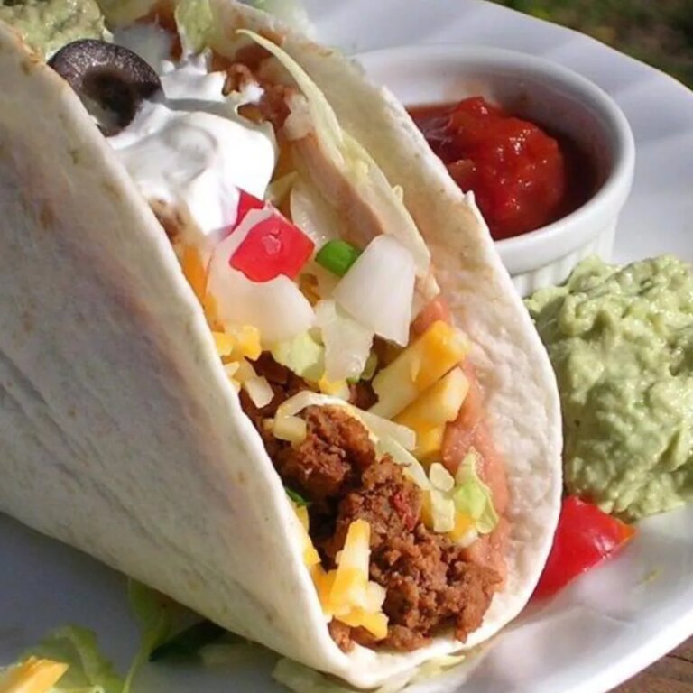 Close up view of a double decker taco served with salsa and guacamole on a plate