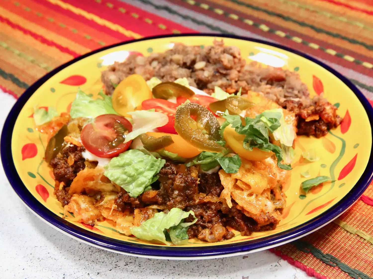Portion of taco casseole with ground beef, cherry tomatoes, and chili served on thick colorful plate
