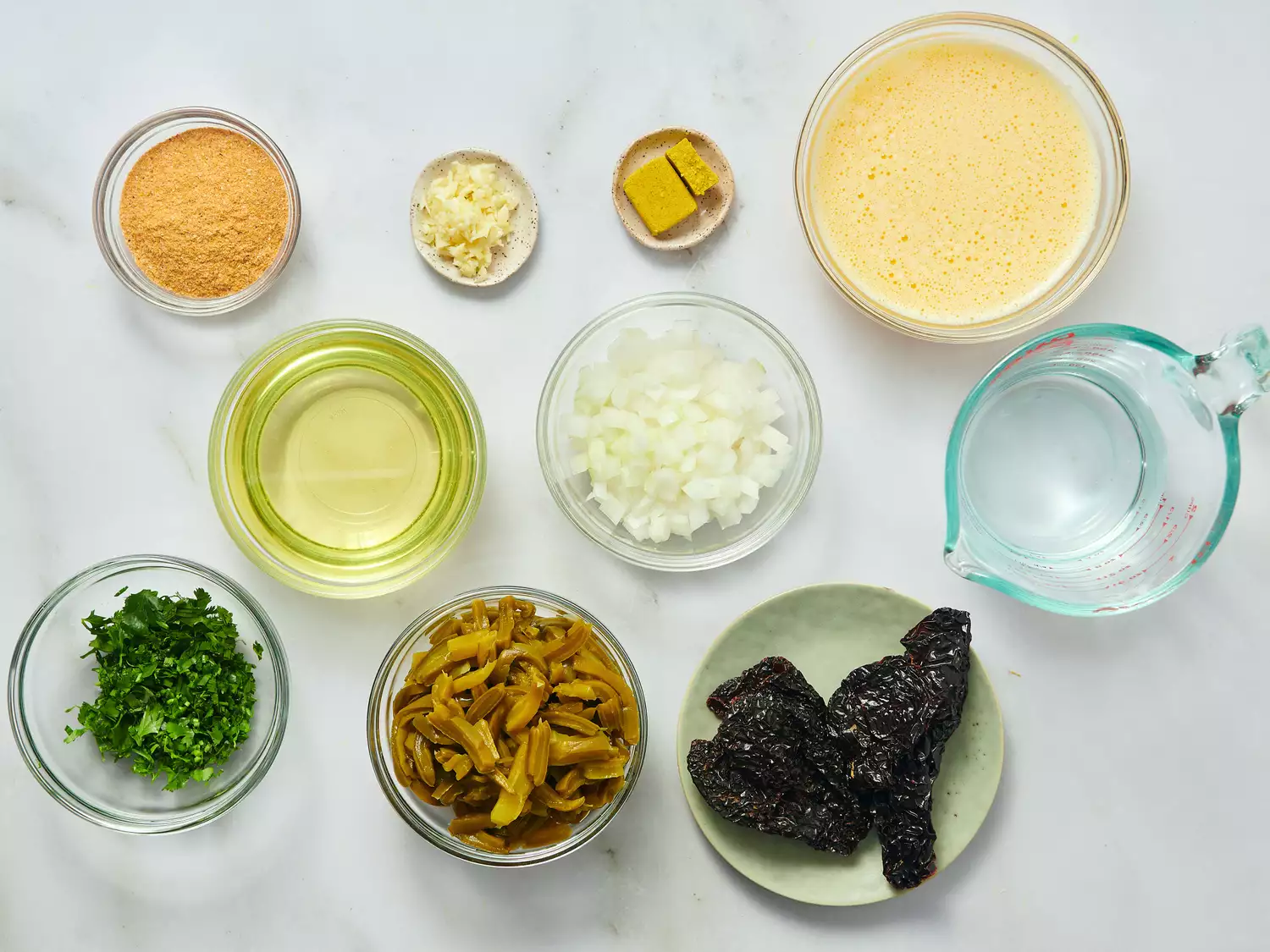 Ingredients arranged on a surface, including broth, diced onion, herbs, dried chilies, and liquids