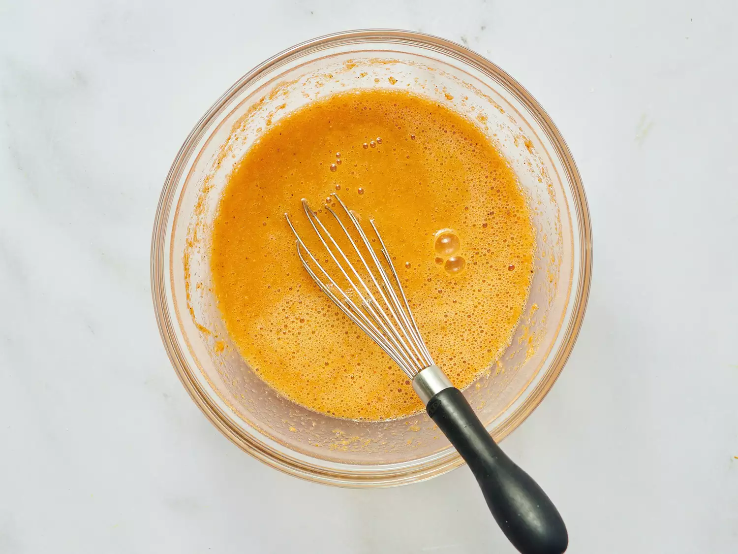 A whisk in a bowl with a blended yellow-orange liquid