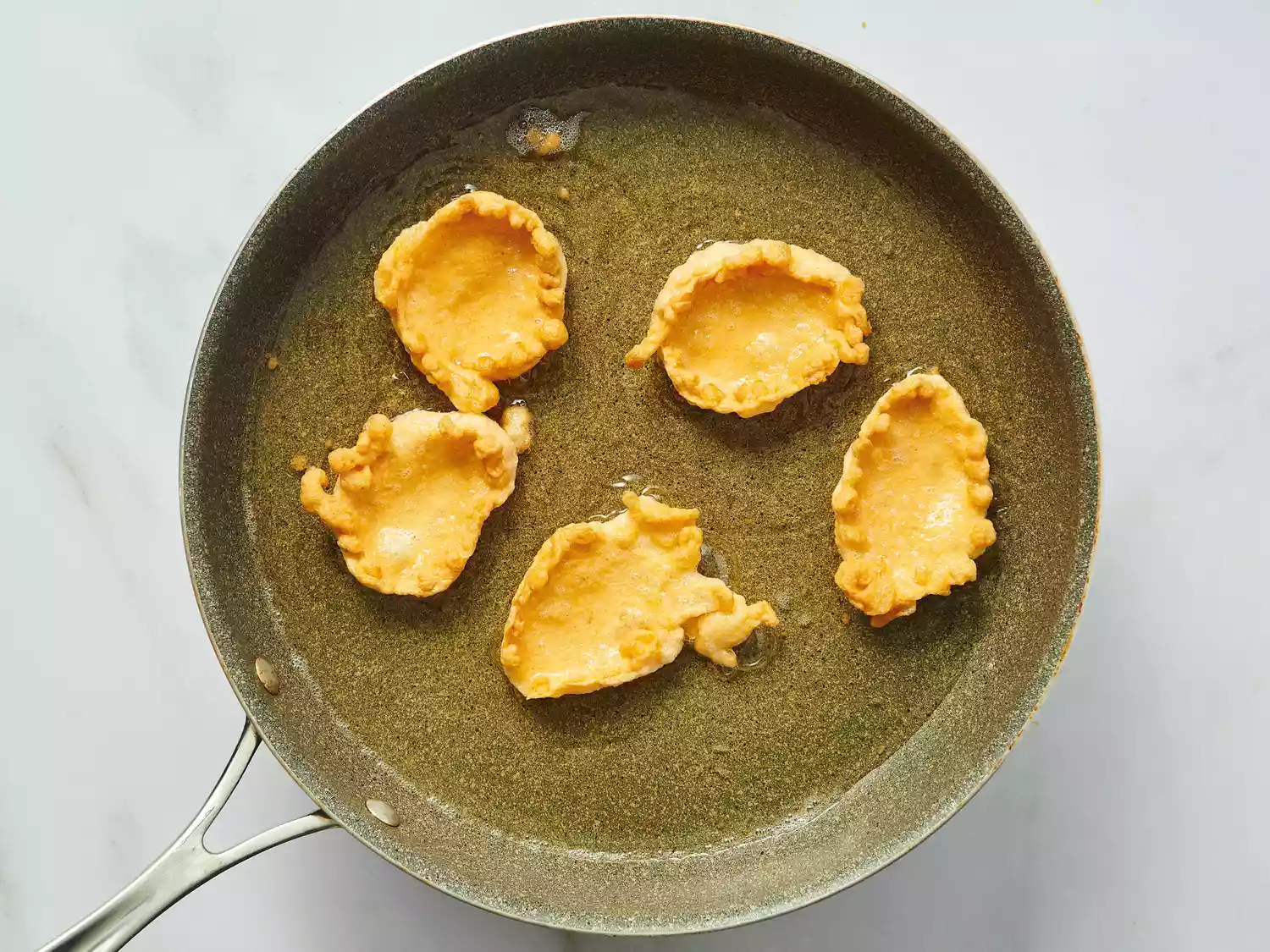 Five shrimp cakes frying in a pan on a stovetop