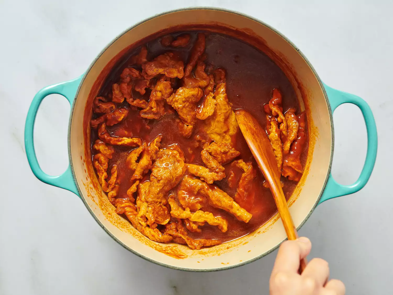 Cooking shrimp tortas in a pot, hand stirring with a wooden spoon