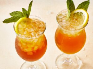 Two tall glasses of long island ice teas garnished with mint and fresh lemon