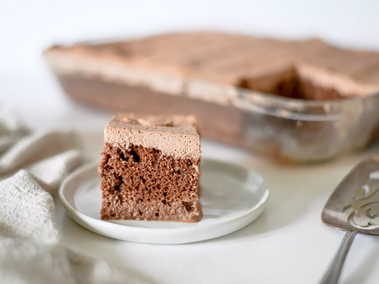 Piece of chocolate tres leches cake on plate with whole cake in the background