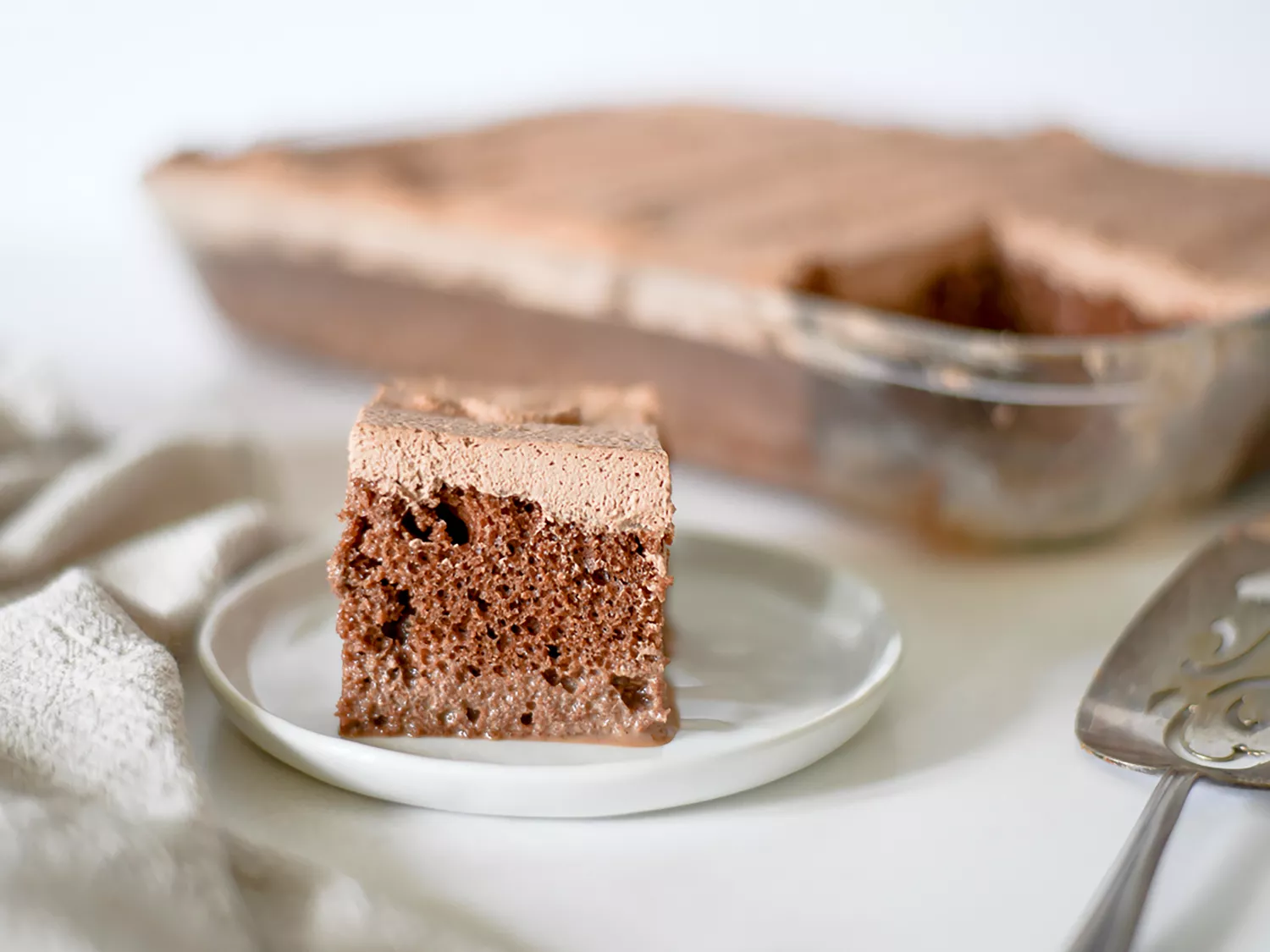 Piece of chocolate tres leches cake on plate with whole cake in the background