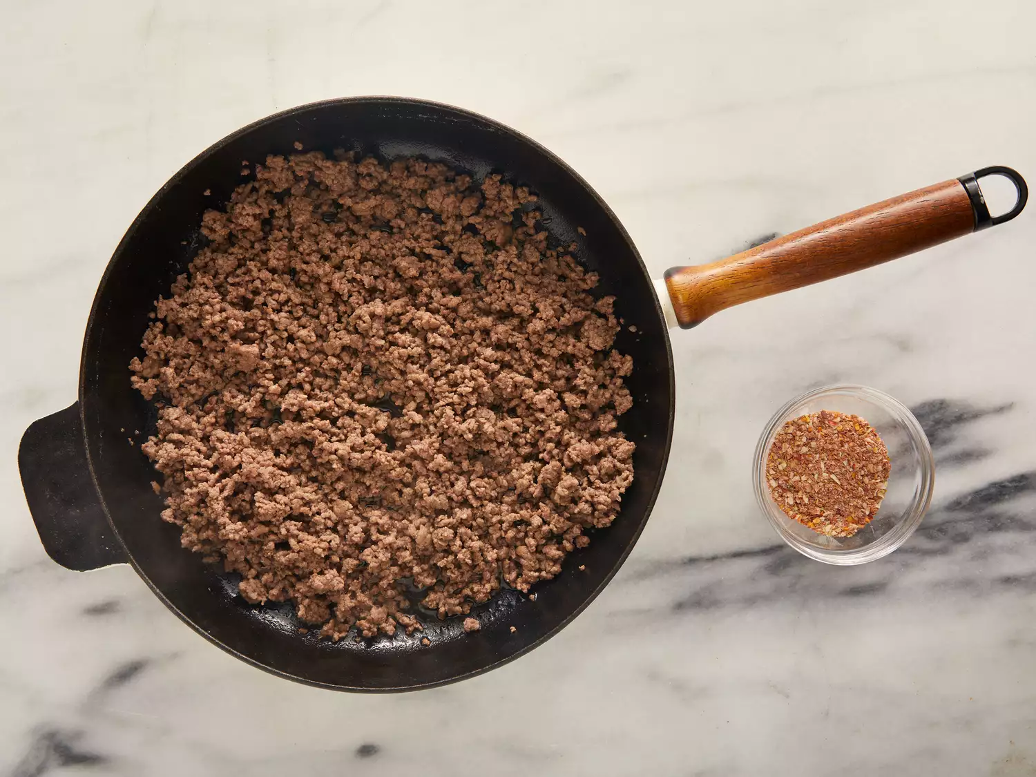 Ground beef in skillet and a small bowl of taco seasoning next to it