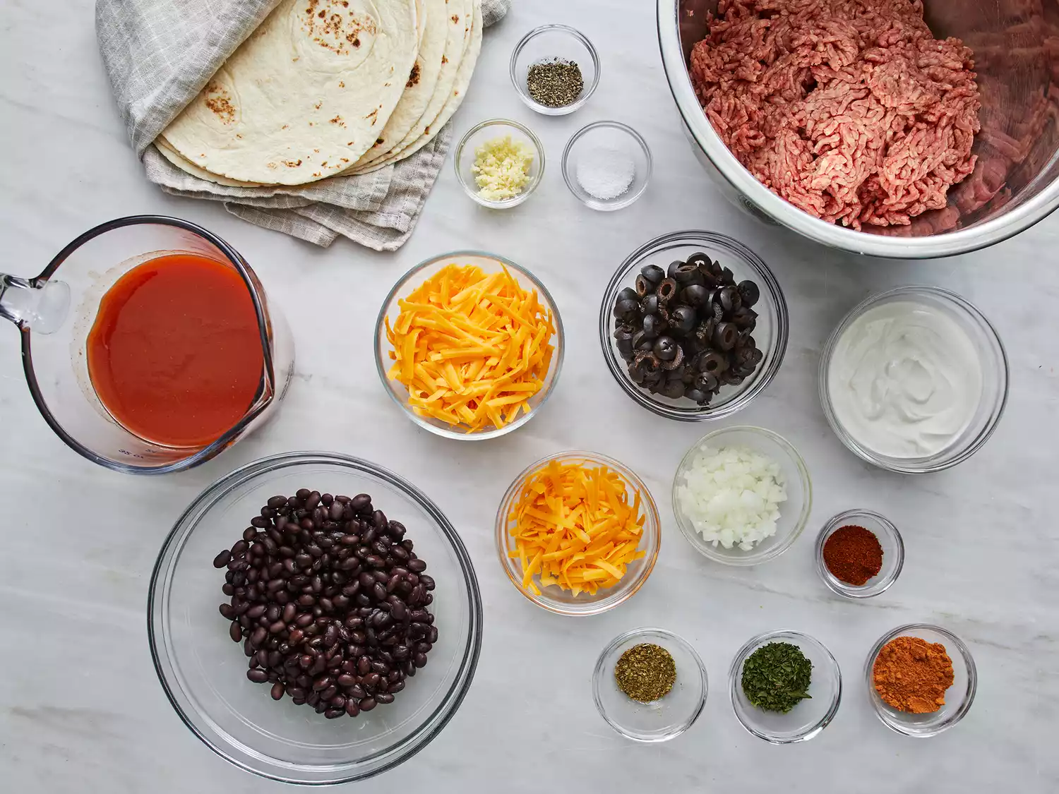 a top down view of all ingredients gathered for beef enchiladas. All sitting on a marble countertop. 