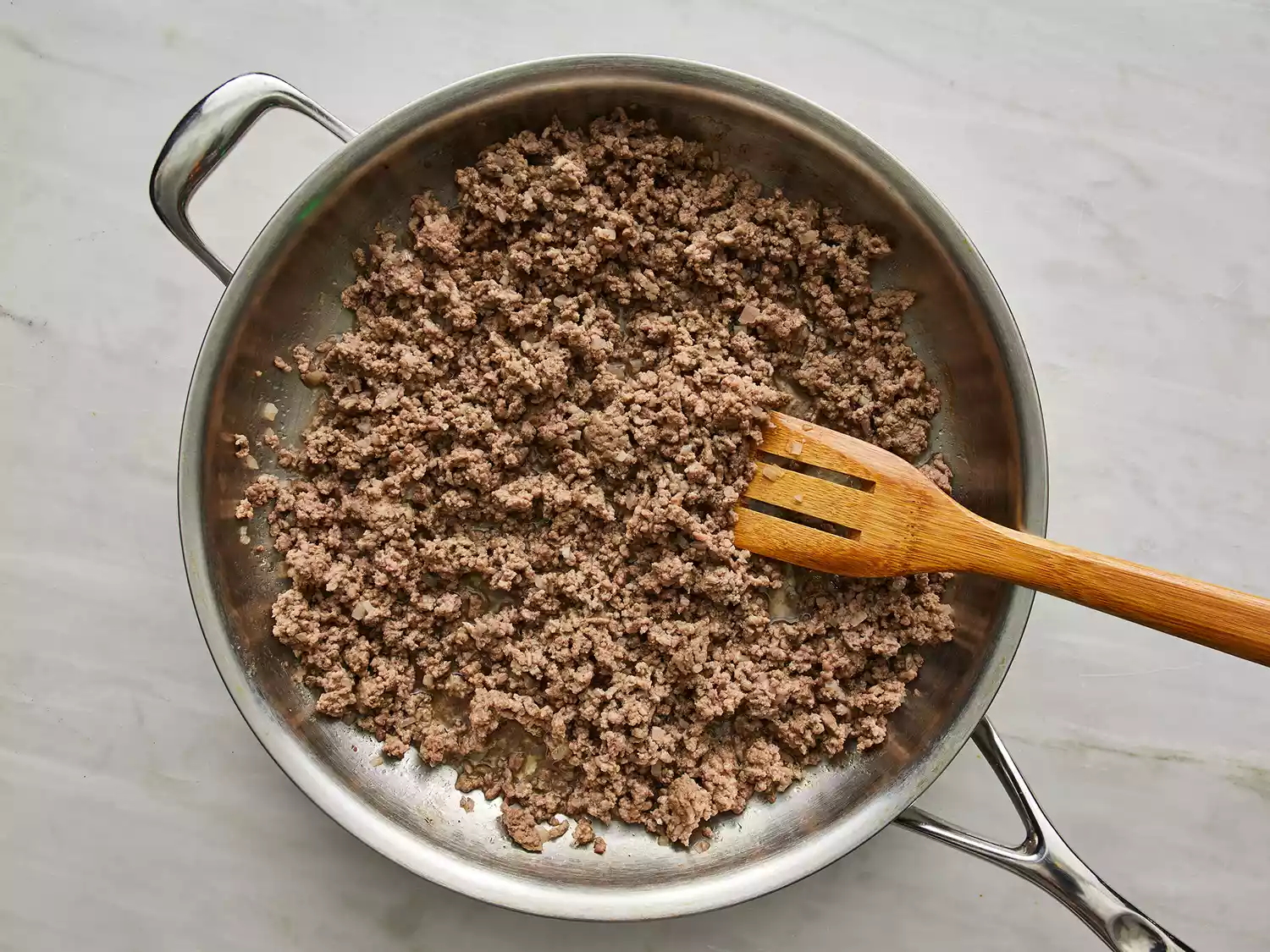 a top down view of ground beef and onions being browned in a large skillet. 