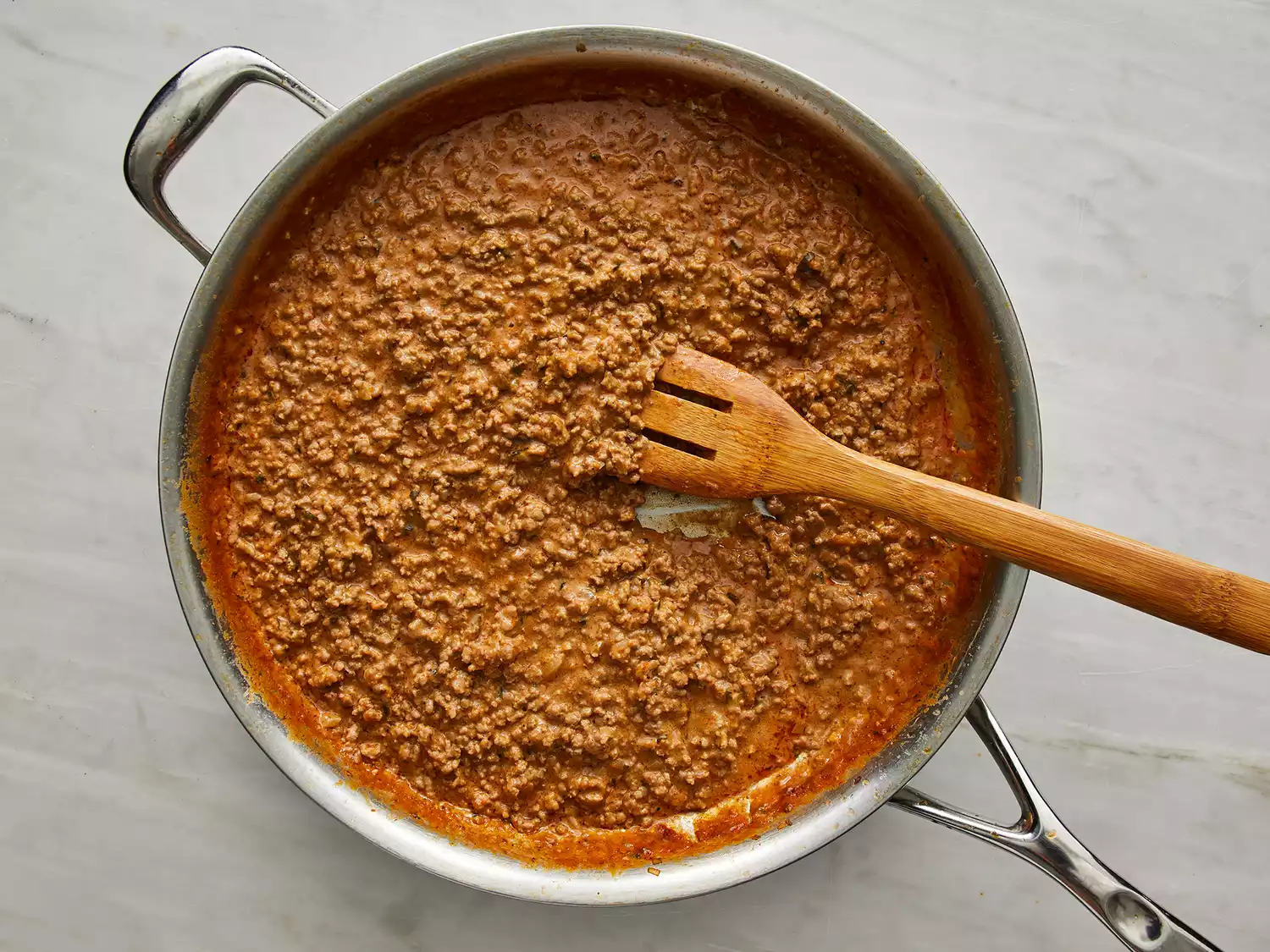 a top down view of enchilada sauce and cheese stirred into ground beef and onion mixture in a large skillet. 