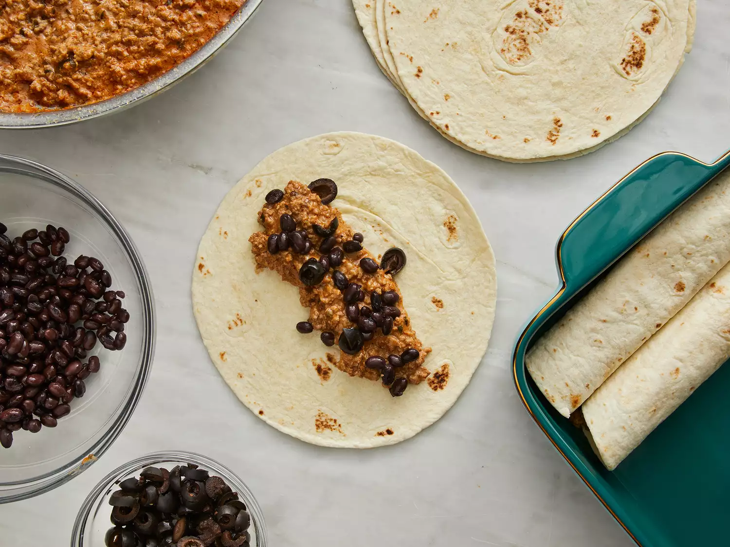 a top down view of beef enchiladas being rolled and put into a prepared baking dish. 