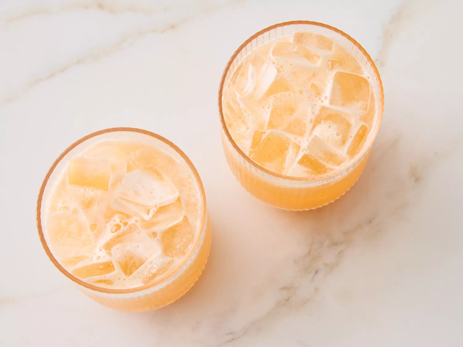 Two glasses of a beverage with ice cubes on a marble surface